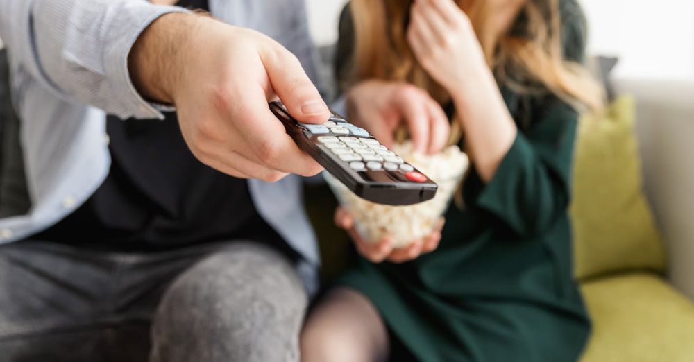 Remote - A couple enjoying a relaxing movie night, sitting on a sofa with popcorn and a TV remote.