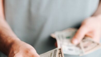 Cost - Close-up of an unrecognizable man holding dollar bills with a blurred background indoors.