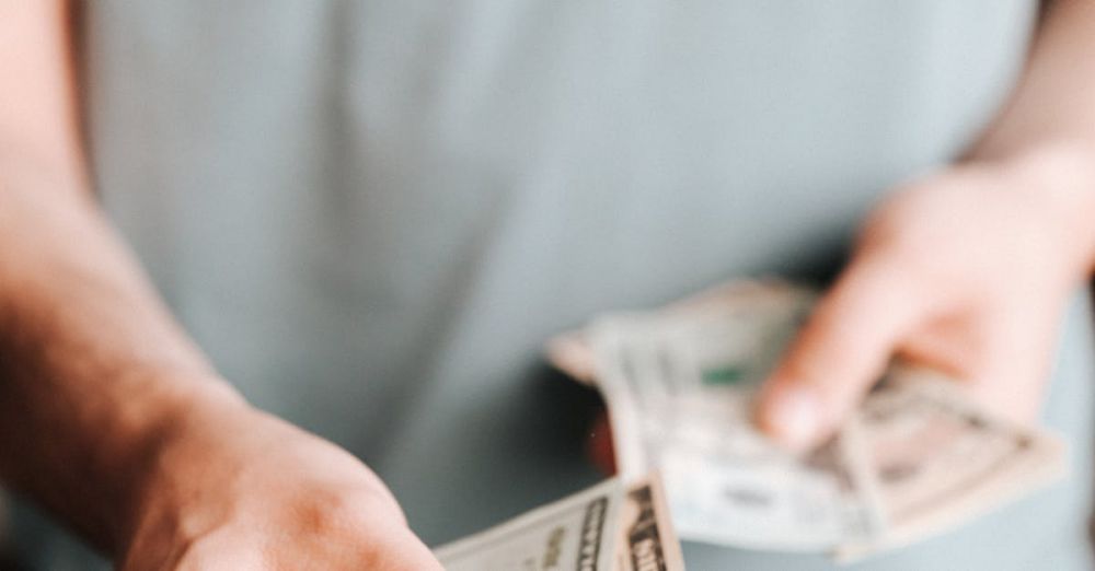 Cost - Close-up of an unrecognizable man holding dollar bills with a blurred background indoors.