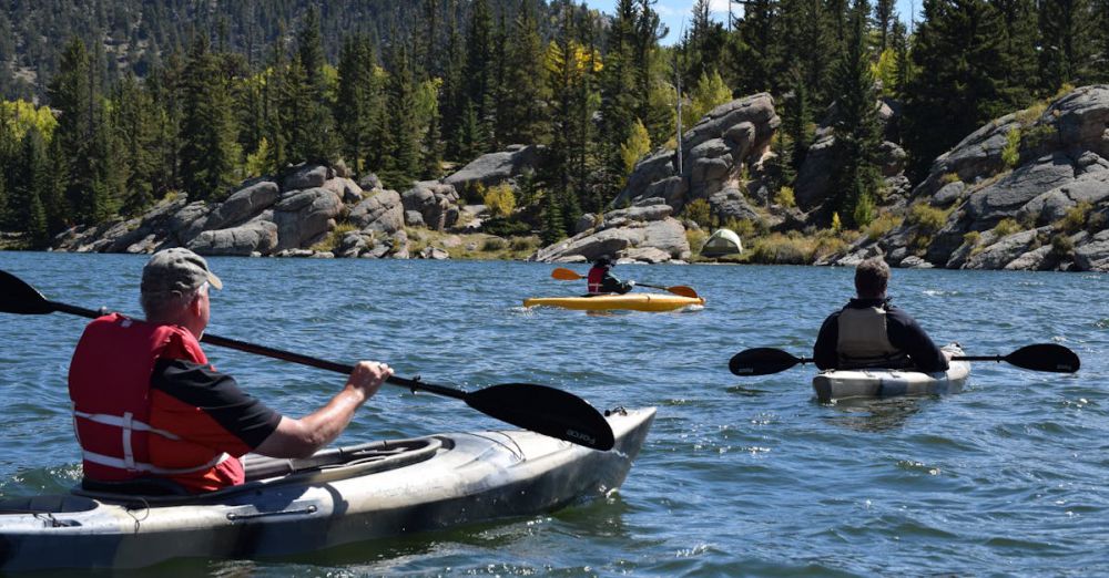 Canoeing - Three people kayaking on a picturesque lake surrounded by rocky terrain and evergreen trees.