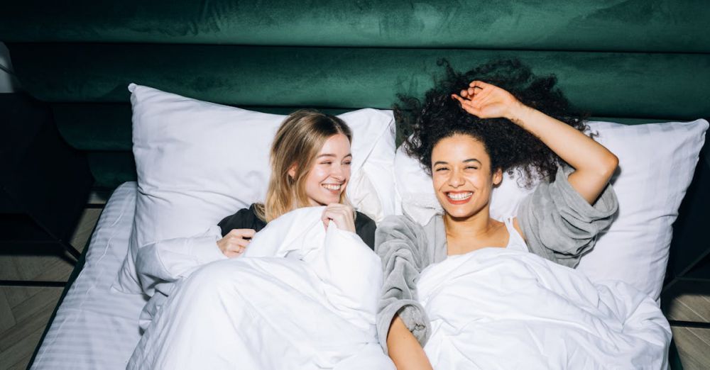 Best Time - Two smiling young women enjoying a fun sleepover with laughter and warmth in a cozy bedroom.