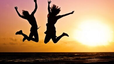 Activities - Silhouettes of two people joyfully jumping on a beach during a vibrant sunset.