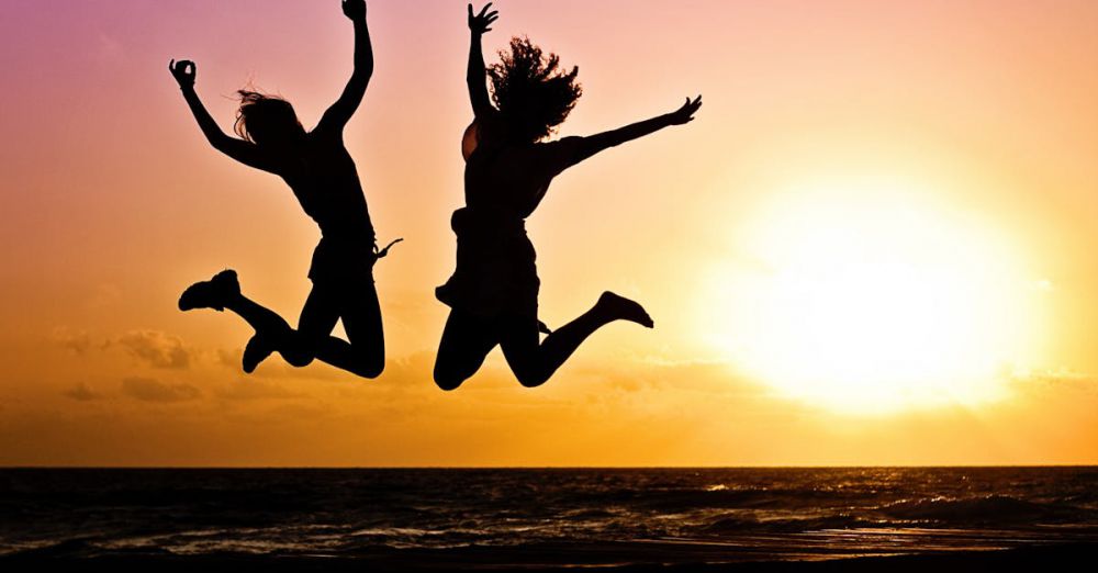 Activities - Silhouettes of two people joyfully jumping on a beach during a vibrant sunset.