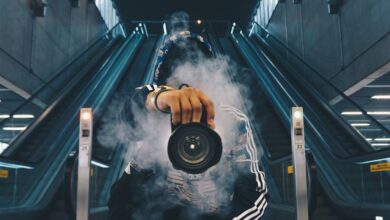 Photography - Person holding a camera in a smoke-filled urban setting with escalators.