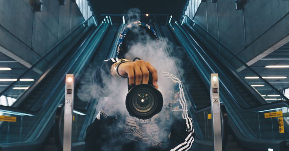 Photography - Person holding a camera in a smoke-filled urban setting with escalators.