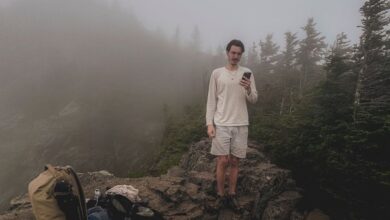 Solo Travelers - A solo male hiker stands on a rocky mountain with fog enveloping the alpine forest, emphasizing solitude and adventure.