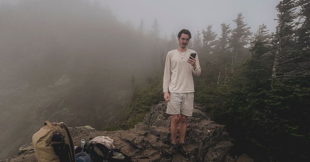 Solo Travelers - A solo male hiker stands on a rocky mountain with fog enveloping the alpine forest, emphasizing solitude and adventure.