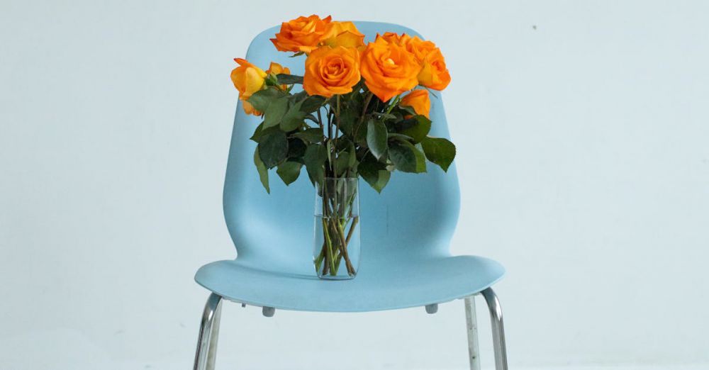 Year-Round - Modern blue chair featuring a vibrant vase of orange roses in minimalist decor.