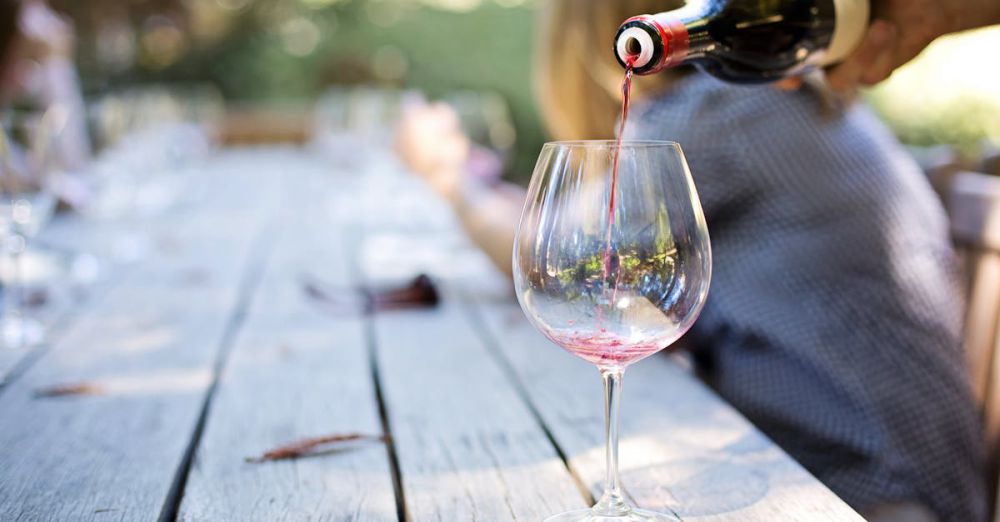 Food Tours - A hand pouring red wine into a glass on an outdoor table, creating a relaxed atmosphere.