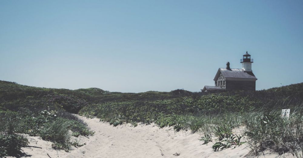 Photography Tours - Scenic view of Block Island Lighthouse with sandy path and lush green dunes under blue sky.