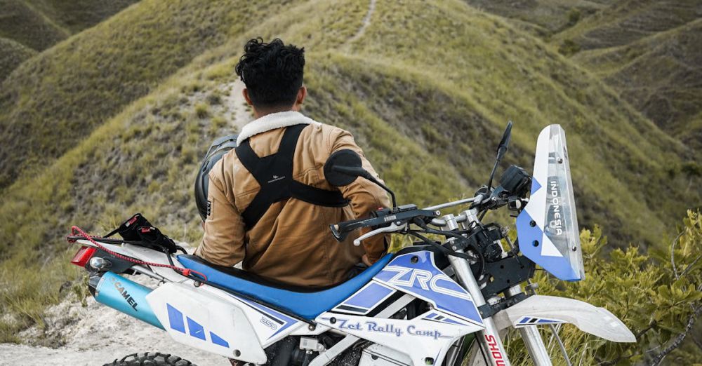 Solo Tours - Rider with motorcycle enjoys a panoramic view over grassy hills under cloudy skies.