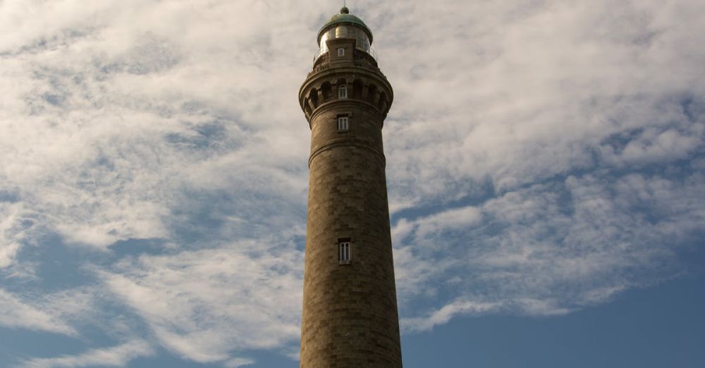 No Guide - A scenic view of Plouguerneau Lighthouse set against a dramatic cloudscape in Brittany, France.