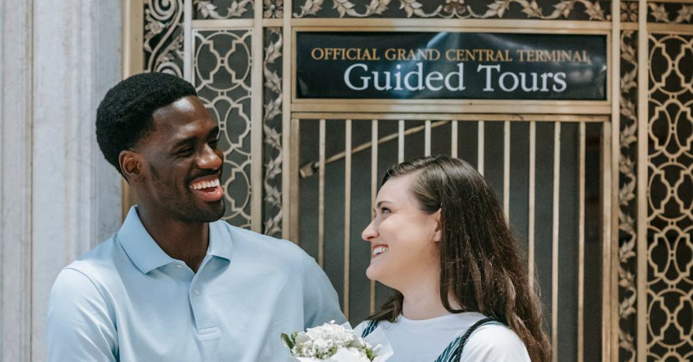 Guided Tours - Smiling couple in front of Grand Central Terminal, holding flowers, showcasing love and summer joy.