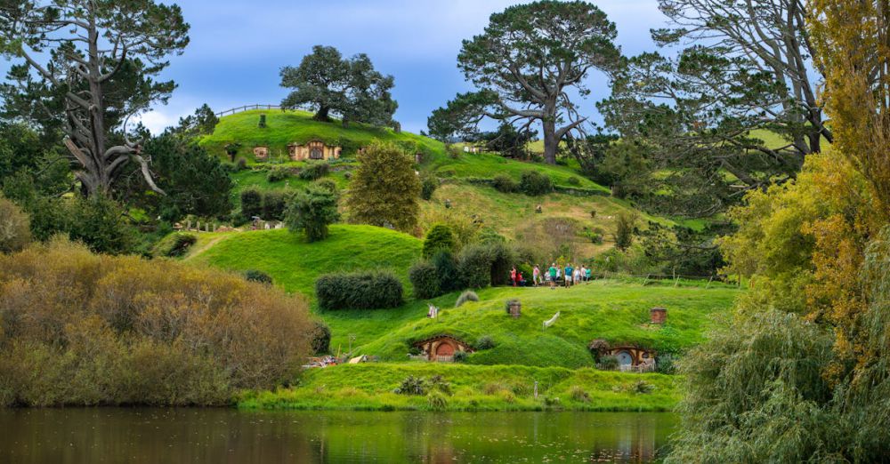 Culture Tours - Lush green landscape of Hobbiton with iconic hobbit holes and serene lake reflecting the vibrant scenery.