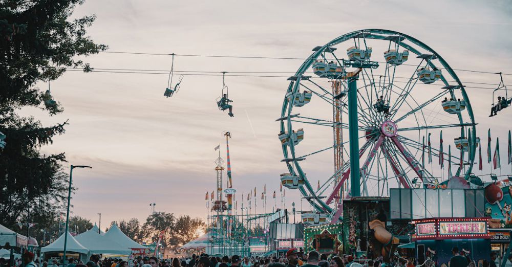 Festival Tickets - Crowd enjoying an amusement park with Ferris wheel and rides at sunset.