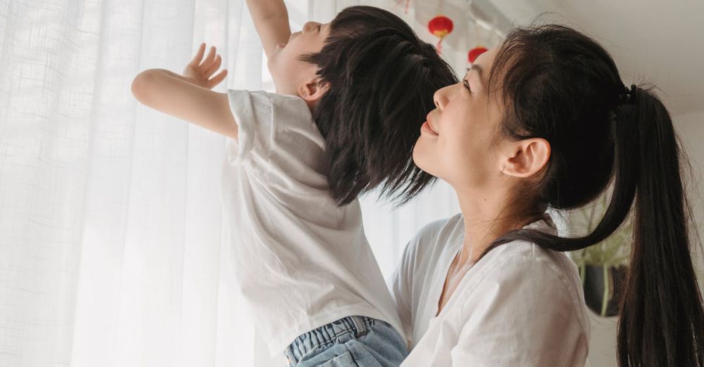 Family Festivals - Asian mother holding son as he reaches for red lanterns in a warm indoor setting.