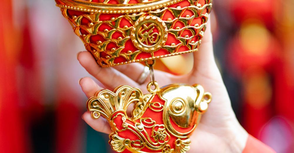 Festival Choices - Crop anonymous female touching traditional ornamental red and golden decoration with fish and sycee hanging in local street market during Chinese New Year holidays