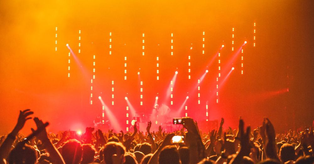 Fans - Energetic crowd at a live concert with bright stage lights and hands raised in celebration.