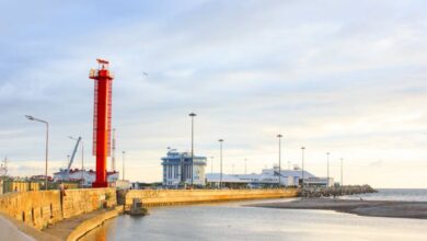 Fishing Guides - Beautiful view of a red lighthouse on a seashore against a calm ocean backdrop at sunset.