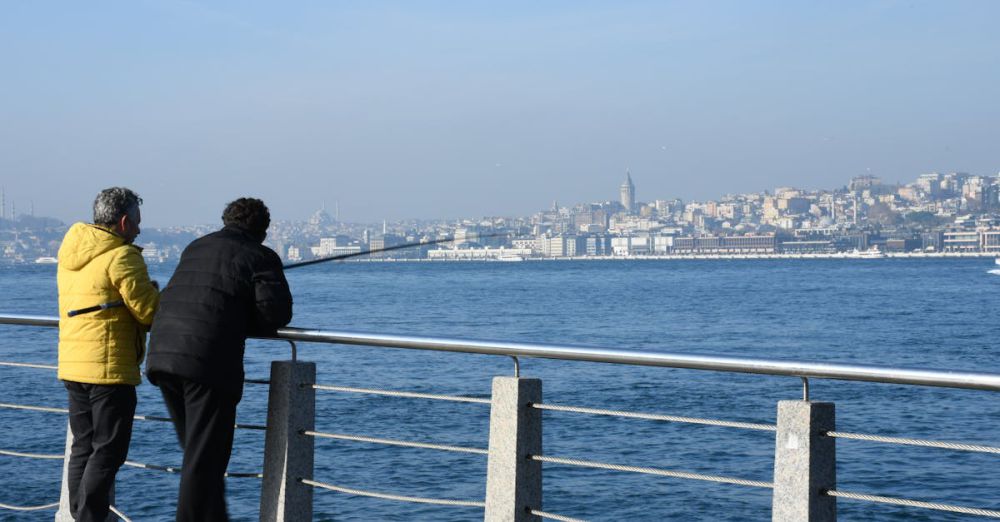 Winter Fishing - Two individuals fishing by the shore overlooking a city skyline, capturing a serene scene.