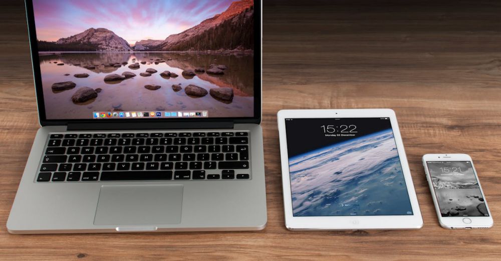 Devices - Modern workspace showcasing Apple laptop, tablet, and smartphone on a wooden desk.