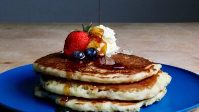 Maple Syrup Tours - Stack of fluffy pancakes topped with syrup, strawberries, blueberries, and cream on a blue plate.