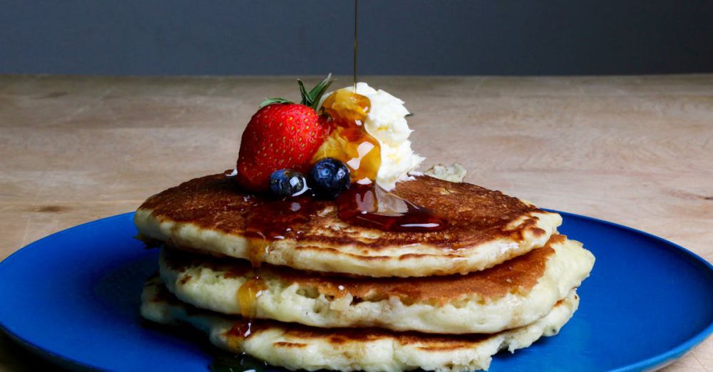 Maple Syrup Tours - Stack of fluffy pancakes topped with syrup, strawberries, blueberries, and cream on a blue plate.