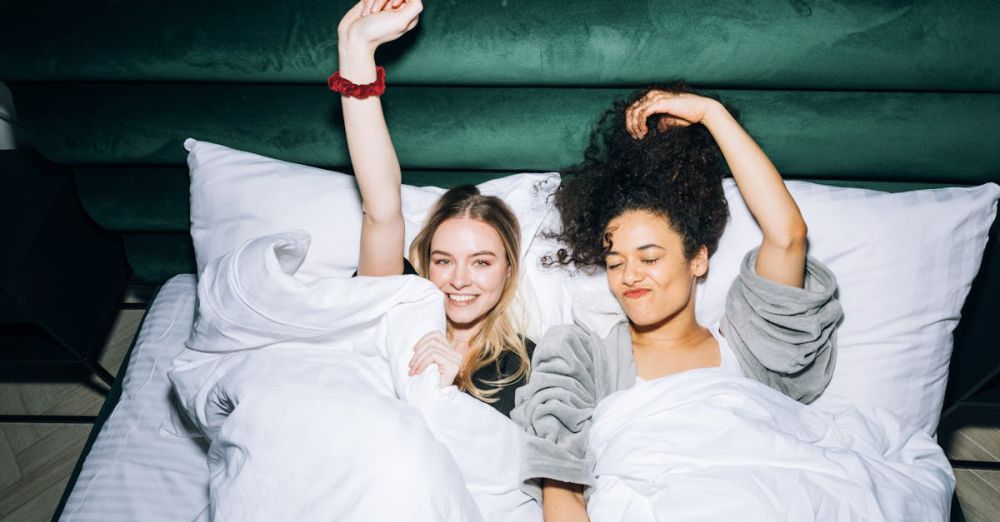 Best Time - Two happy friends enjoying a relaxing time in bed with white linens, exuding joy and friendship.