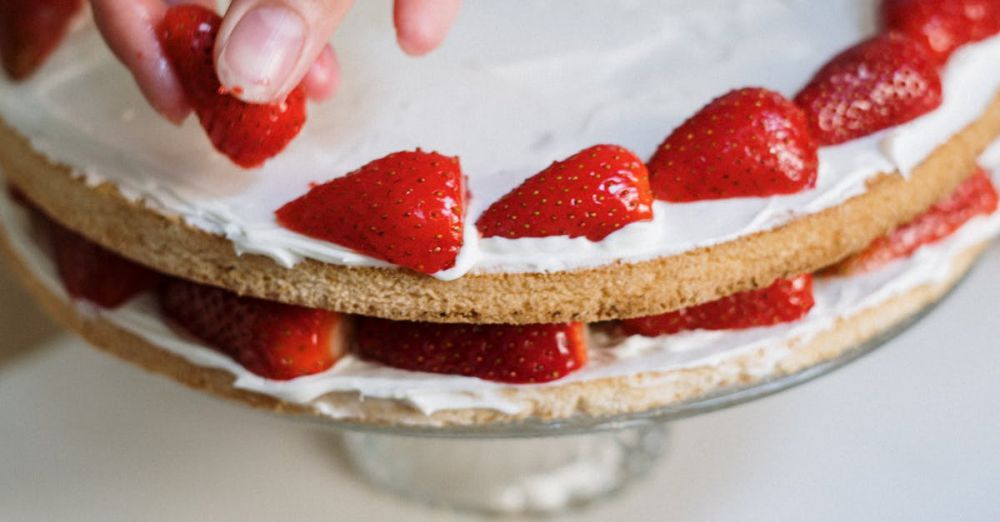 Home Syrup Making - Hand placing strawberries on a delicious homemade layer cake with fresh blueberries nearby.