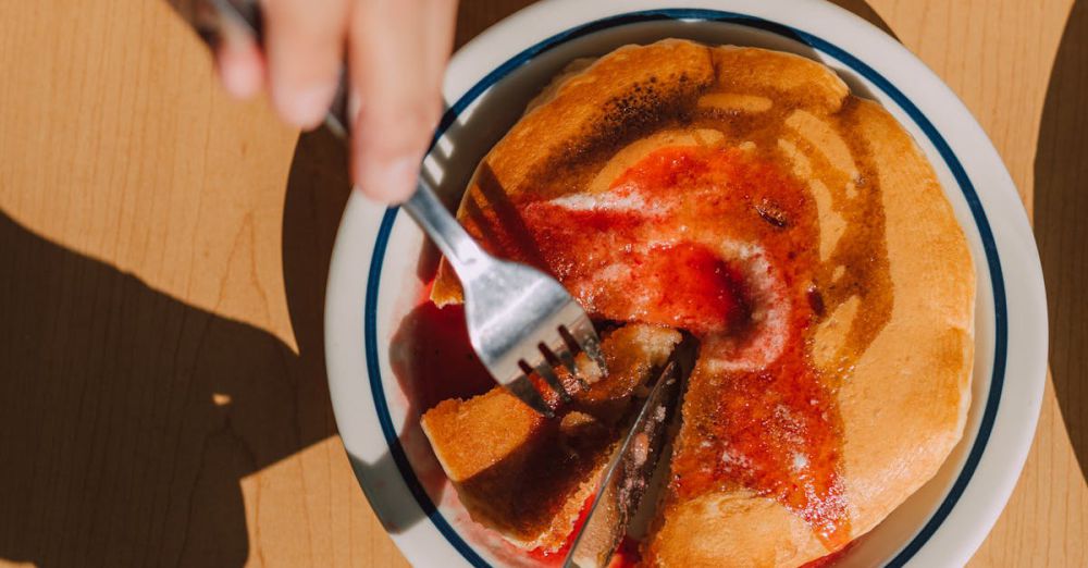 Maple Syrup Pairing - Overhead shot of hands slicing a pancake with syrup in a well-lit setting.