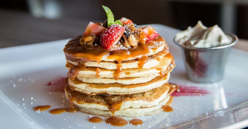 Pancakes - Mouthwatering pancakes with strawberries, nuts, and syrup on a plate.