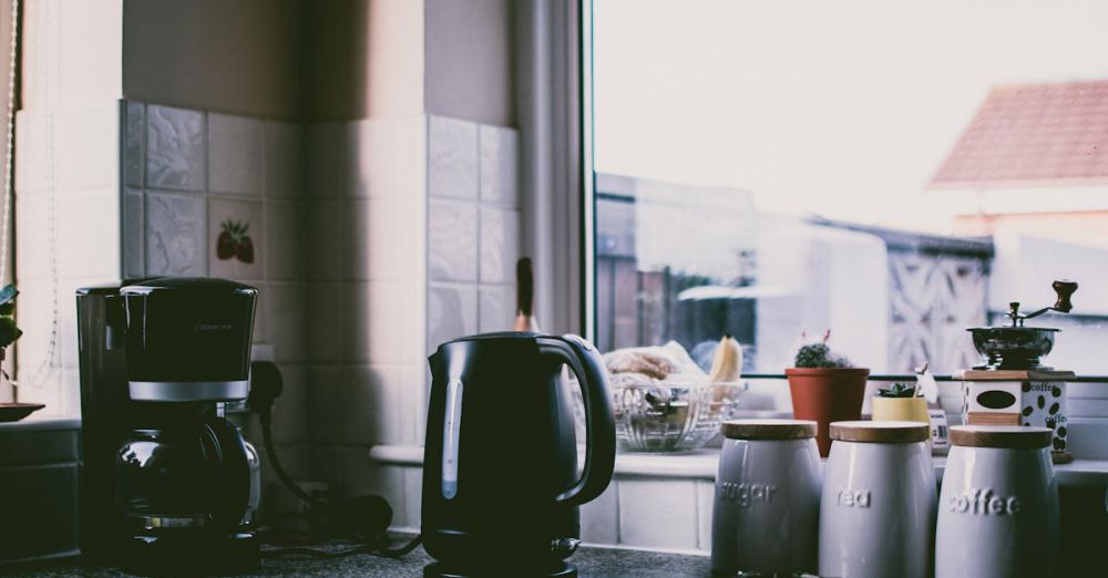 Appliances - Cozy kitchen scene with coffee maker, kettle, and jars on a sunny counter.