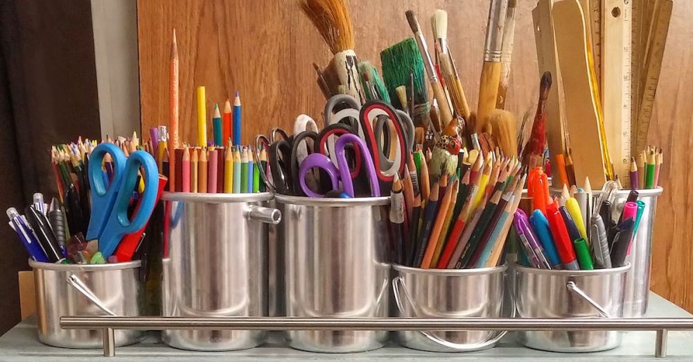 Pens - A diverse collection of art supplies in metallic buckets on a wooden table.