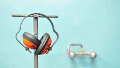 Safety - Close-up of earmuffs hanging on a metal stand in front of a teal wall.