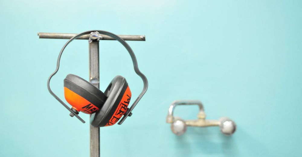 Safety - Close-up of earmuffs hanging on a metal stand in front of a teal wall.