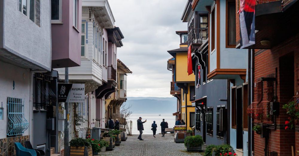 Outdoor Exploration - Picturesque European street with colorful buildings leading to a serene waterfront on a cloudy day.