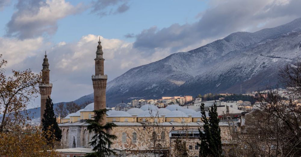 Architecture Photography - A serene winter view of the historic Ulu Mosque with snowcapped mountains and cloudy skies.