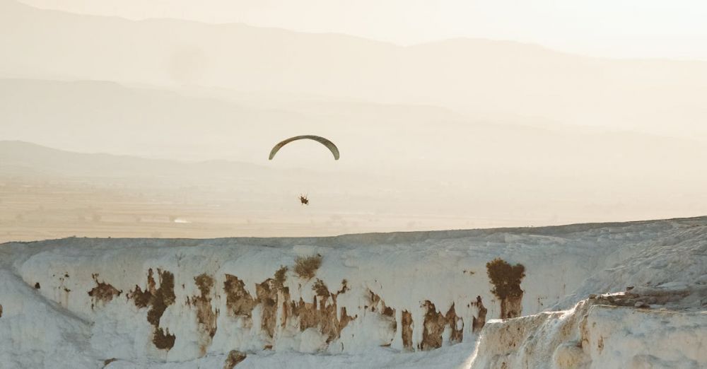 Hot Springs - A paraglider soars above the stunning white terraces of Pamukkale at sunset.