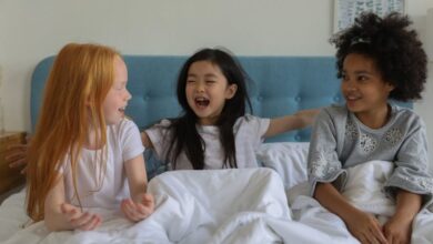 Best Time - Three happy girls bonding and laughing together in bed during a cozy sleepover.