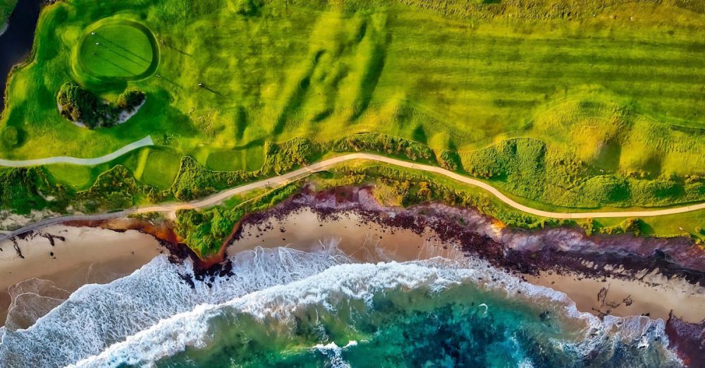 Golf Resorts - Stunning aerial view of a coastal golf course beside a vibrant beach with waves crashing onto the shore.