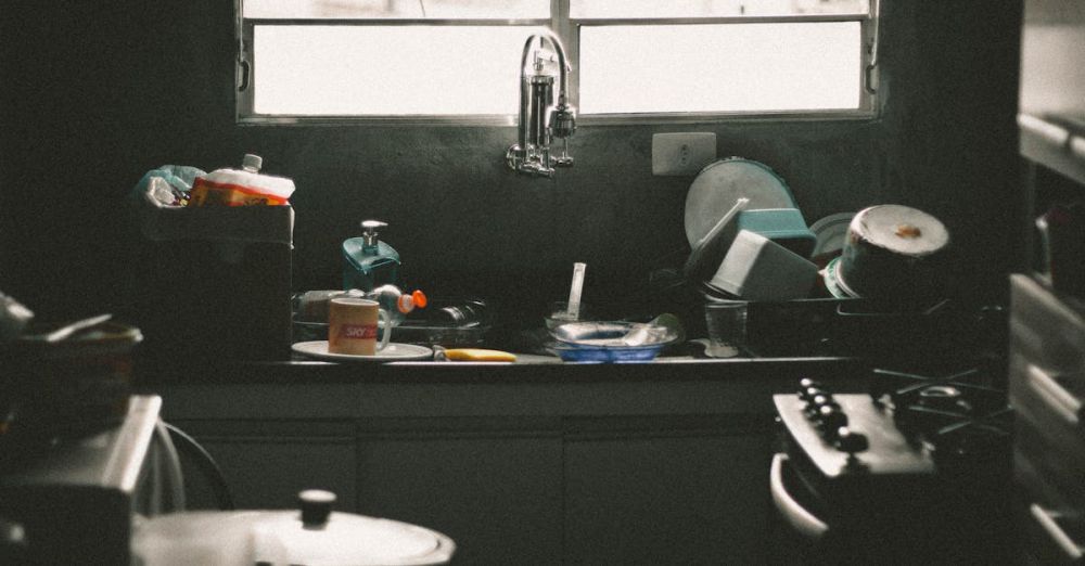 Dishwashers - A cluttered kitchen sink filled with dirty dishes and utensils near a window, creating a messy home interior scene.