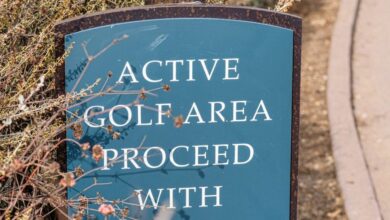 Golf Safety - Sign in a golf park warns to proceed with caution, surrounded by foliage.