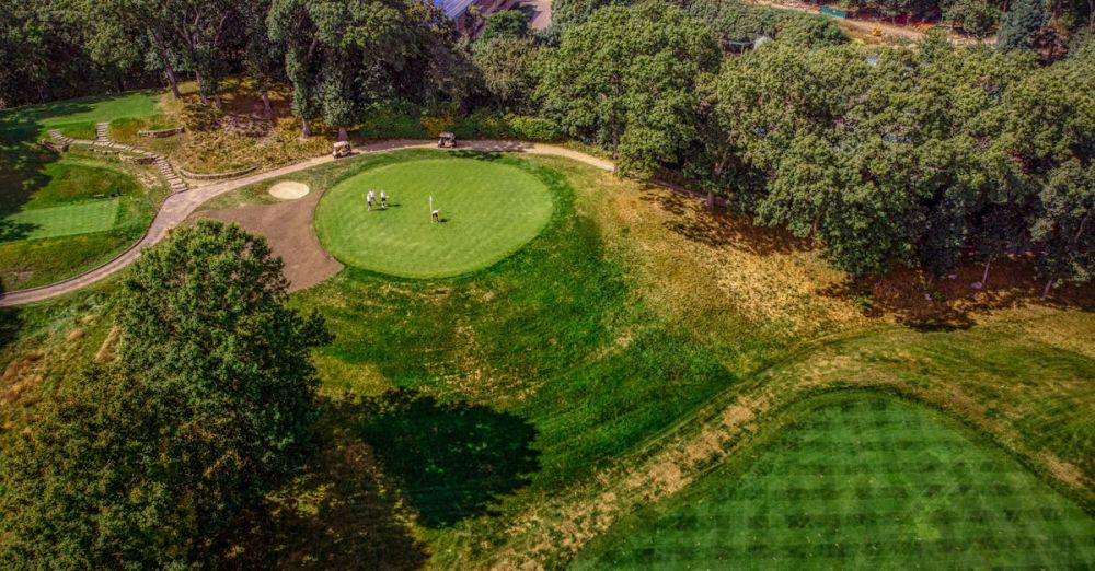 Tournament Courses - Aerial view of a lush golf course surrounded by trees, showcasing the vibrant greens under a sunny sky.