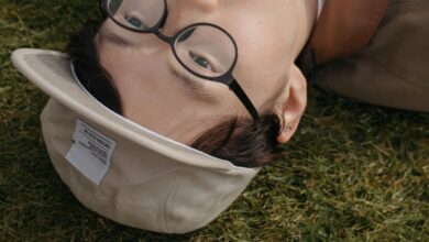 Golf Photography - A playful portrait of a young man lying on grass with a golf ball in his mouth, wearing glasses and a cap.