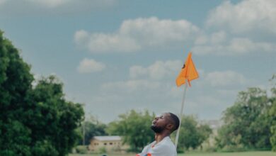 Solo Golf - An adult man sitting on a golf course next to a flag, enjoying a sunny day outdoors.