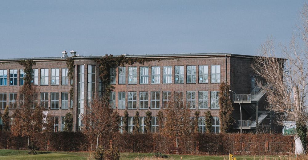 Corporate Golf - A modern building with large windows viewed from a golf course featuring a grassy field and trees.