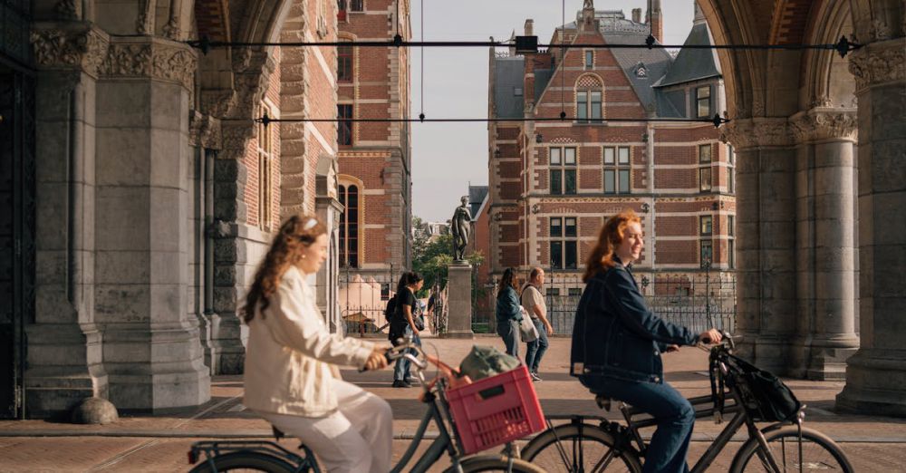 Bike-Friendly Cities - Women cycling under an Amsterdam archway with historical buildings in the background.