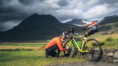 Cycling Tour Preparation - Cyclist adjusting gear on loaded bike in Iceland's rugged landscape under dramatic skies.