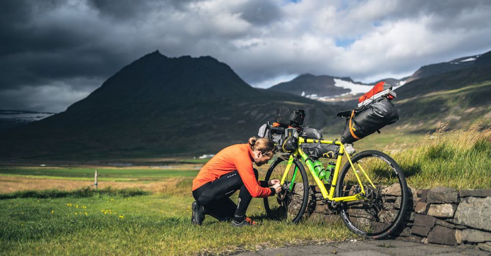 Cycling Tour Preparation - Cyclist adjusting gear on loaded bike in Iceland's rugged landscape under dramatic skies.