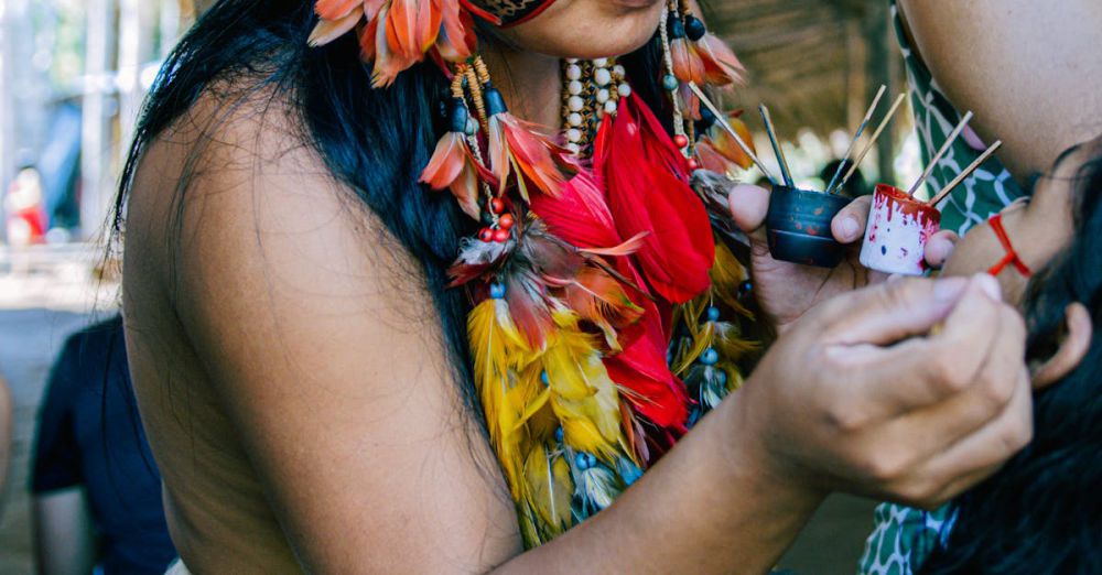 Indigenous Art - Indigenous woman adorned in tribal attire paints another's face during a cultural ceremony.